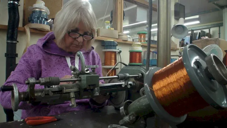 Women grey hair and glasses working at the Fine wire coil winding machine